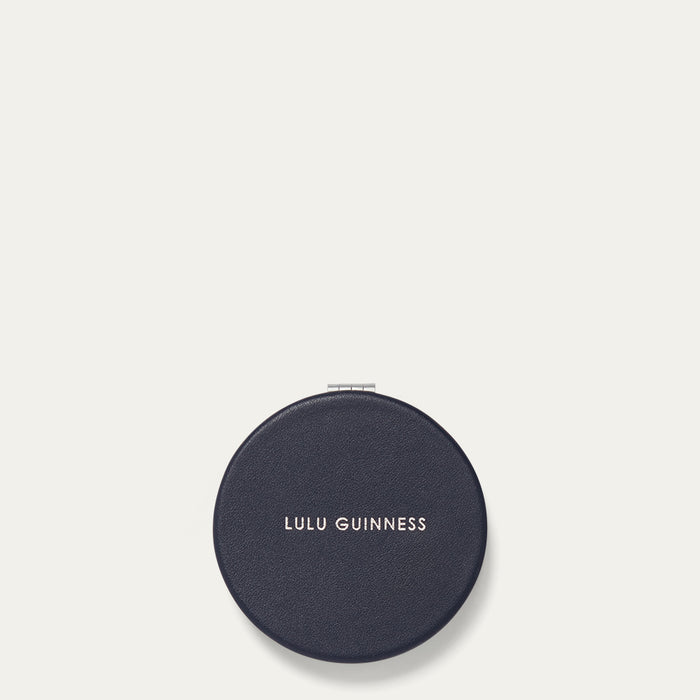 Round navy compact mirror with 'Lulu Guinness' branding on a light gray background