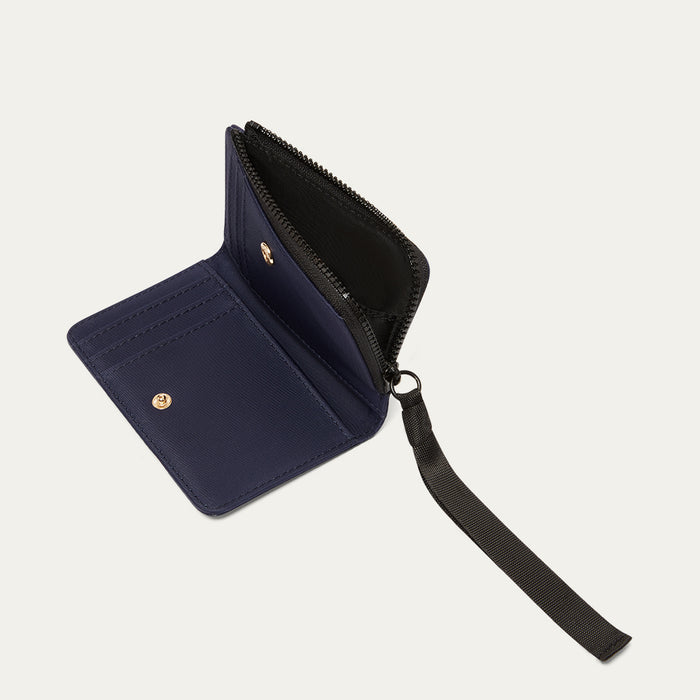 Navy blue wallet with a black ribbon zip pull open on a light grey background