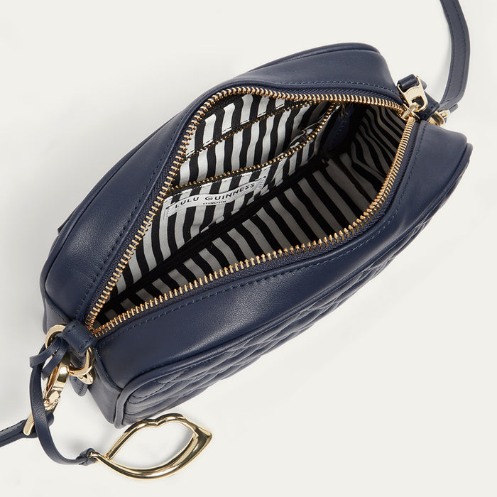 Navy blue leather handbag with gold zipper open revealing a black and white striped lining on a light gray background