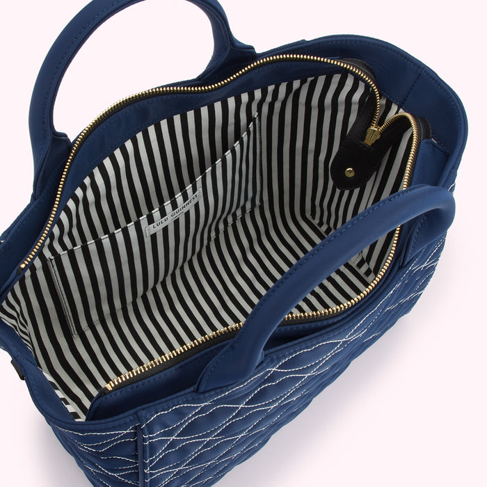 Inside view of a navy blue quilted Lulu Guinness handbag with black and white striped lining and gold zippers.