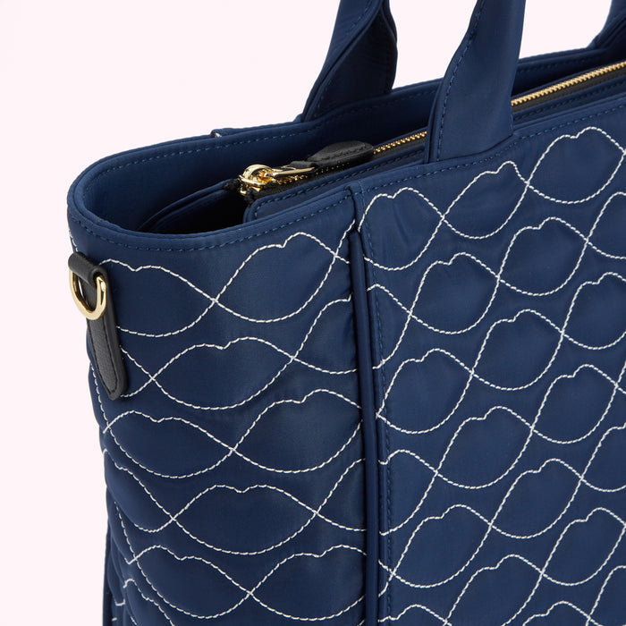 Close-up of a navy blue quilted tote bag with a lip-shaped pattern stitched in white.