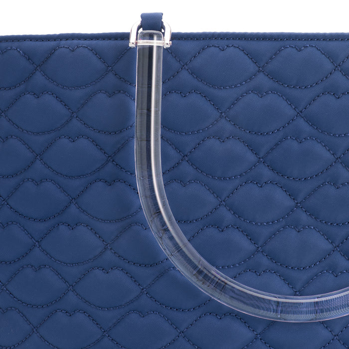 Close-up of a navy blue quilted handbag with a clear acrylic handle; the quilting is patterned with lip shapes.
