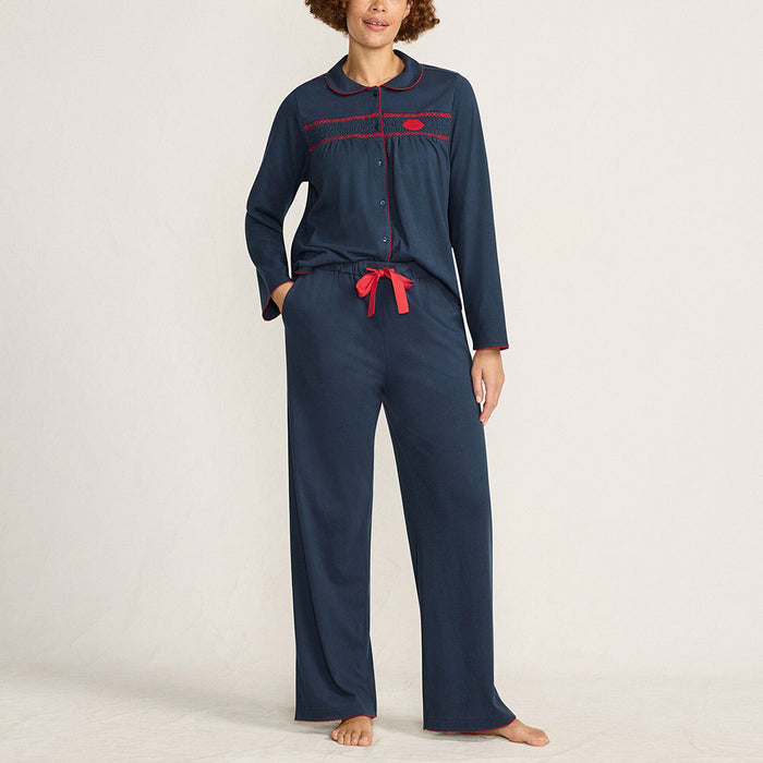Woman in navy pyjamas with red smock detailing and lip motif standing against a plain background.
