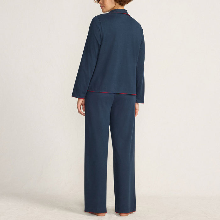 Woman in navy pyjamas with red detailing standing against a plain background.