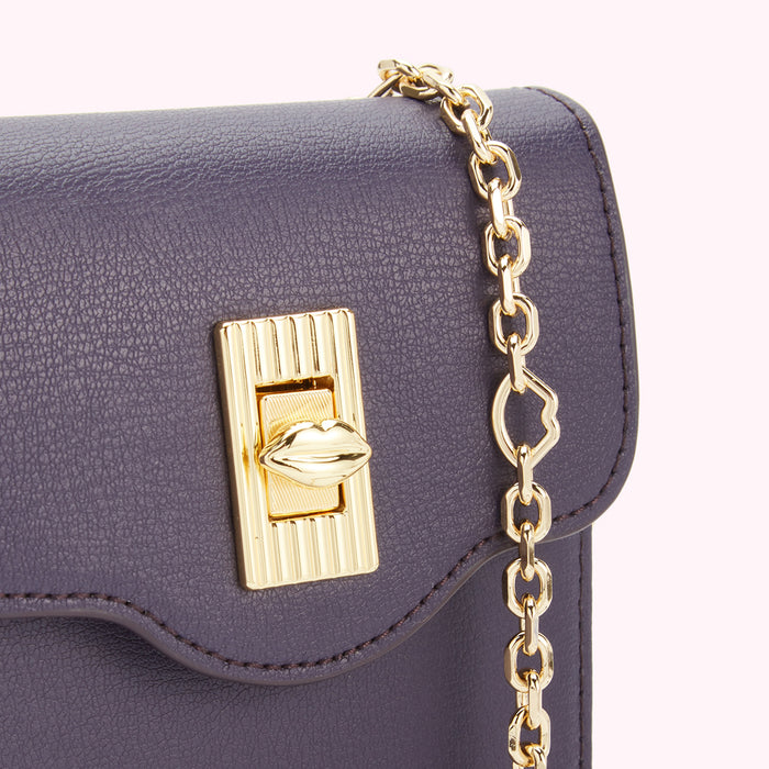 Close-up of a purple textured leather crossbody bag with a gold lip-shaped clasp and chain strap.