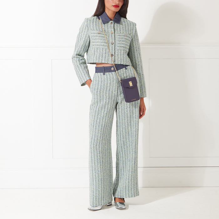 A woman in a light green tweed pantsuit and dark purple crossbody bag against a white background.