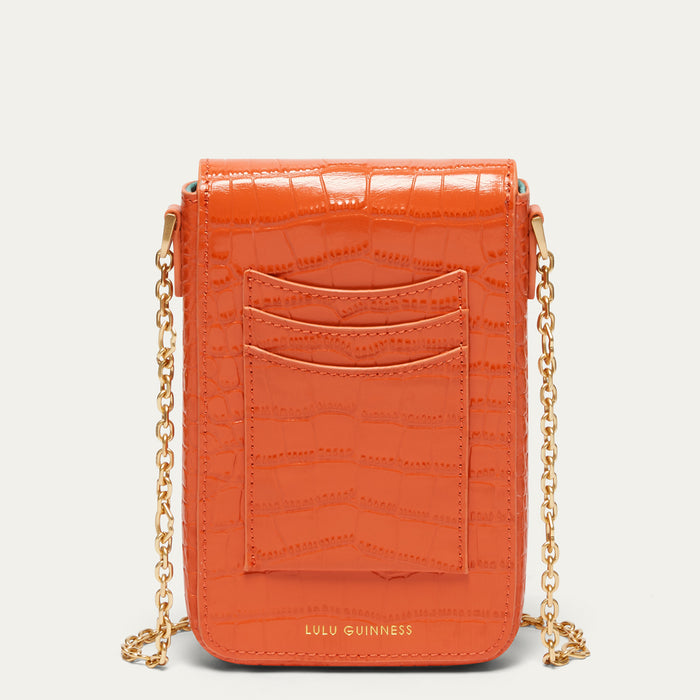 An orange croc affect embossed leather crossbody bag with gold-tone chain straps and the Lulu Guinness logo at the bottom, shown against a light gray background.
