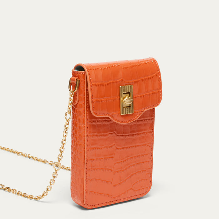 An orange croc affect leather crossbody phone bag with a gold-tone turn-lock clasp and a gold chain strap, shown on a light off-white background.
