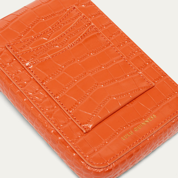 Close-up of an orange croc affect embossed leather bag with card slip pockets and gold 'LULU GUINNESS' logo on a light background.