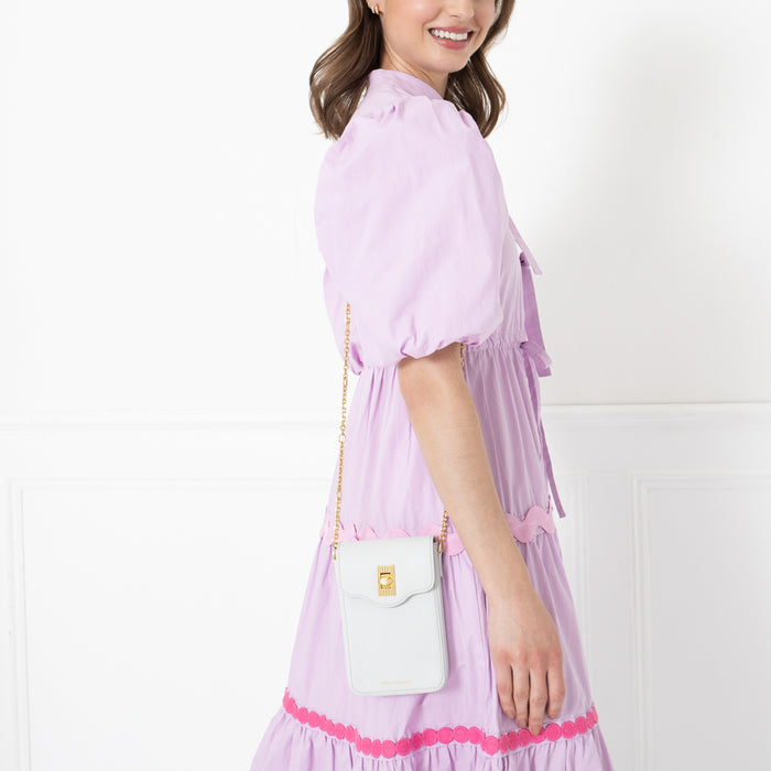 Woman in lavender dress holding light purple crossbody bag with gold chain strap.