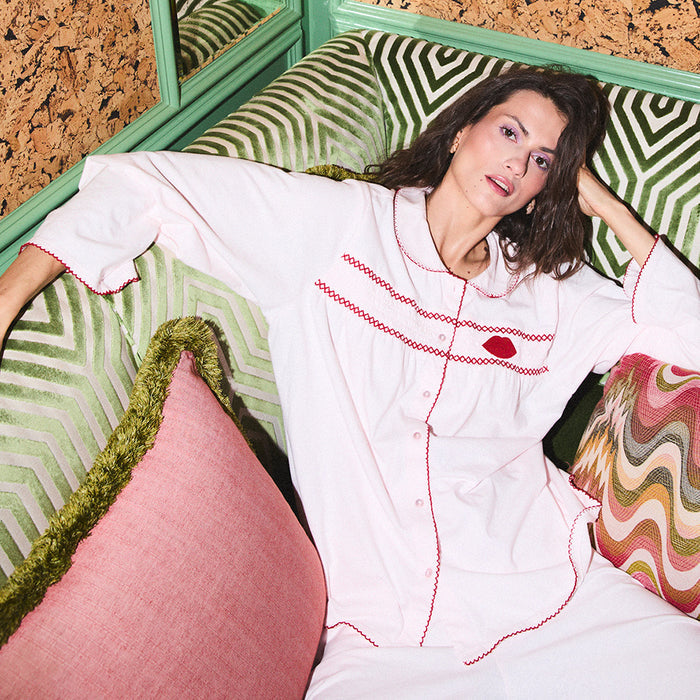 Woman in pale pink pyjamas with red embroidery sitting on a patterned couch.