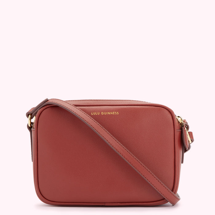 A burnt orange Lulu Guinness crossbody bag with a long strap.