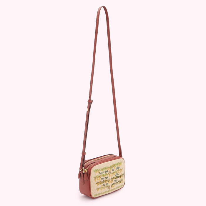 Brown leather crossbody bag with beige embroidered canvas front panel displaying text and floral motifs, against a white background.