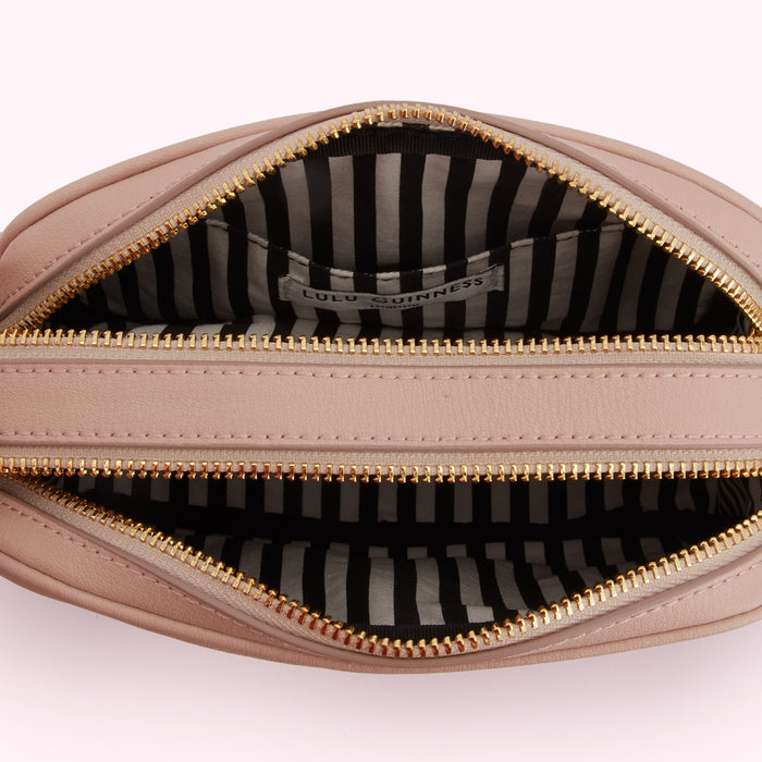 Inside of a pale pink Lulu Guinness crossbody bag showing the black and white striped lining and gold zippers.