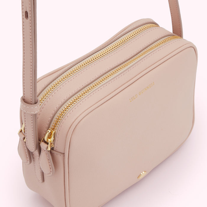 A pale pink Lulu Guinness crossbody bag with two gold zippers.