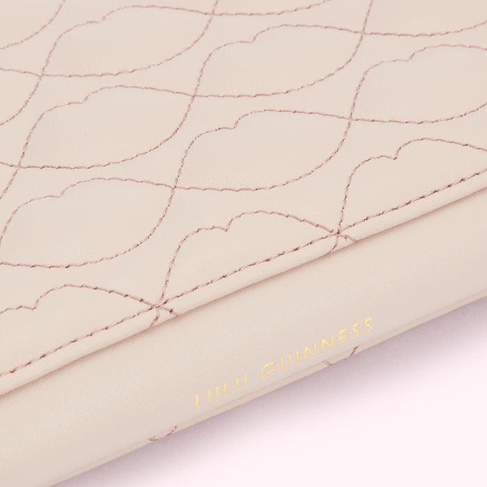 Close-up of a pale pink Lulu Guinness purse with a quilted lip pattern and the brand name subtly embossed on the side.