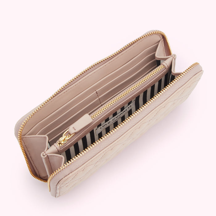 Open blush pink Lulu Guinness quilted zip-around wallet with gold zipper and black and white striped interior.
