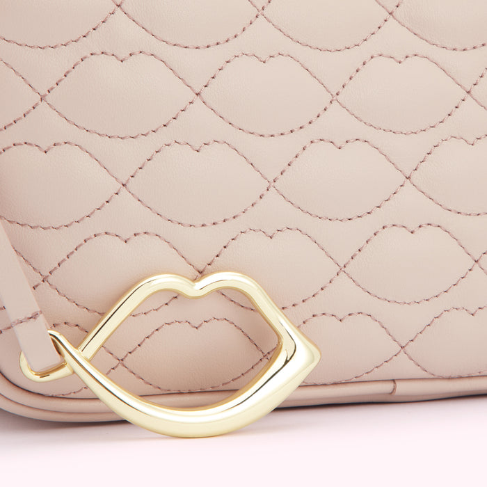 Close-up of a blush pink quilted handbag with a gold lip-shaped detail.