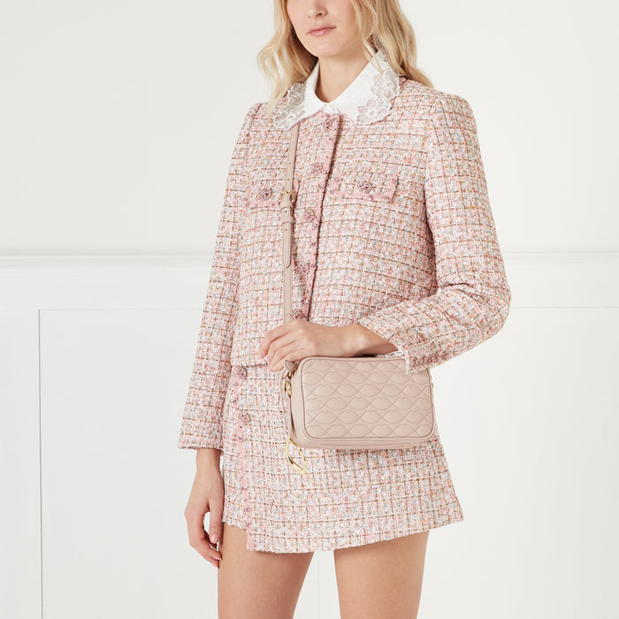 Woman in pink tweed jacket and skirt holding a light pink quilted crossbody bag.