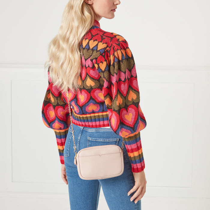 A woman in a heart-print sweater carries a pale pink crossbody bag.