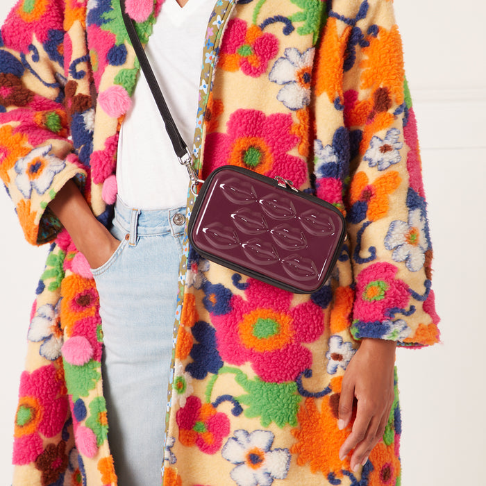 Burgundy crossbody bag with lip-shaped texture, worn over a floral coat.