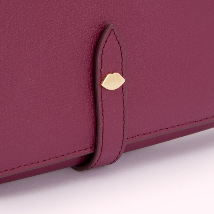 Close-up of a burgundy leather wallet with a gold lip-shaped detail on the strap.