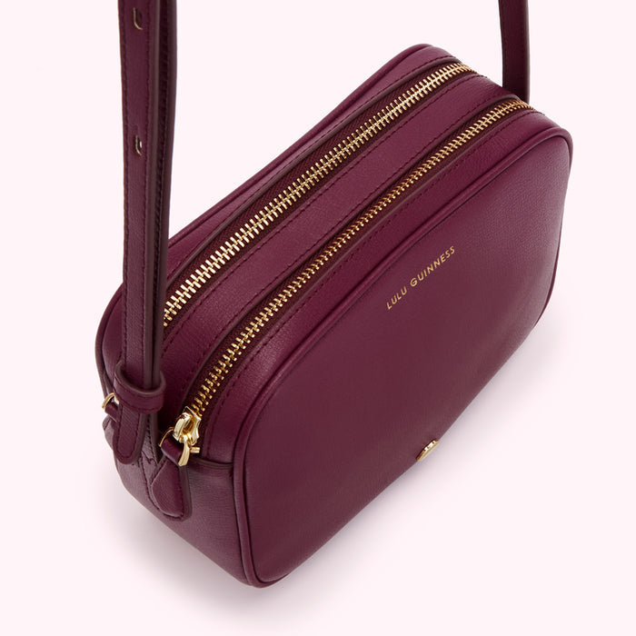 Burgundy Lulu Guinness crossbody bag with gold zippers.