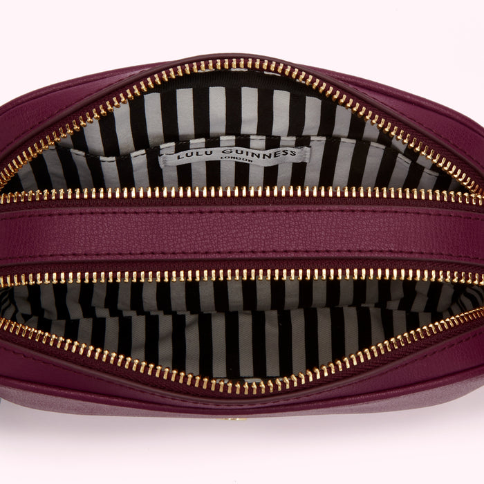 Inside of a purple Lulu Guinness crossbody bag with gold zippers and a black and white striped lining.