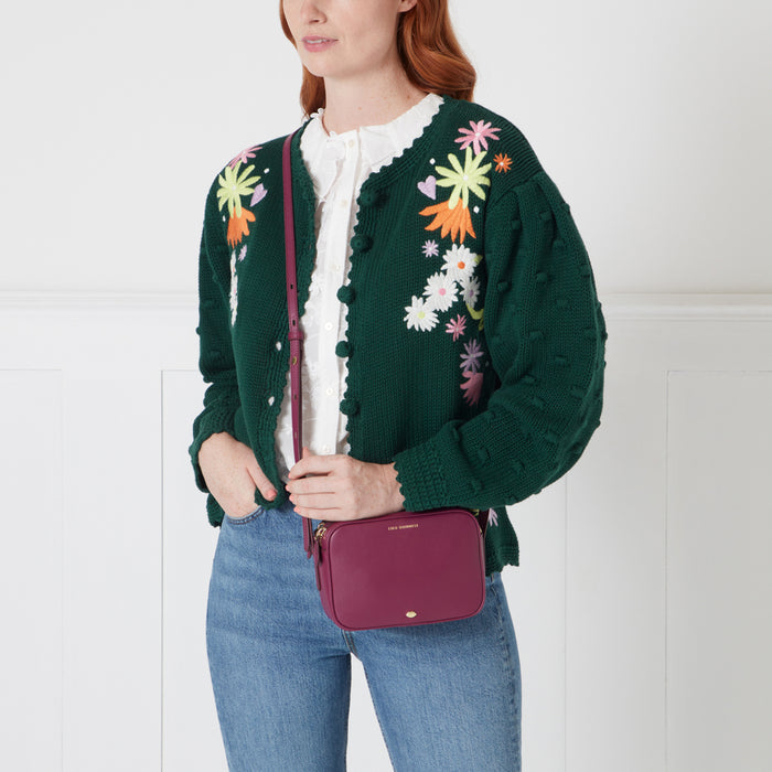 Woman in a green floral cardigan and jeans, wearing a burgundy crossbody bag.