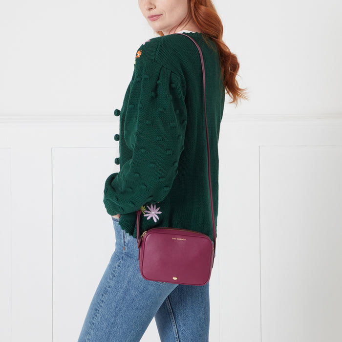A woman wearing a dark green cardigan and jeans carries a dark pink crossbody bag.