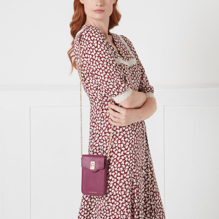 A woman in a burgundy floral dress holds a dark purple crossbody bag with a gold clasp.