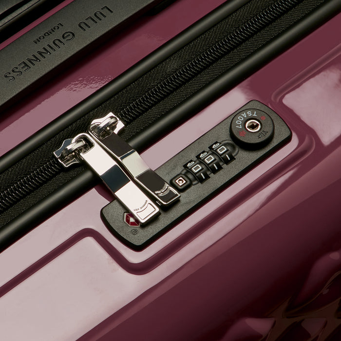 Close-up of a Lulu Guinness suitcase's TSA-approved combination lock and zipper pull. The suitcase is a deep mauve colour.