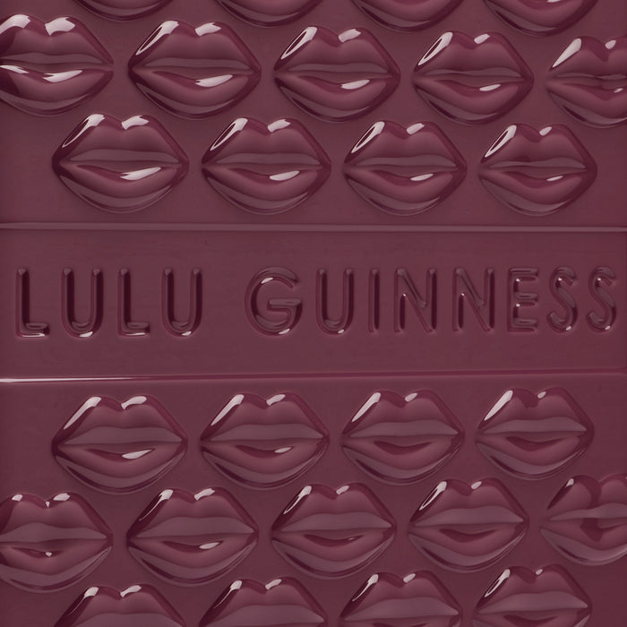 Close-up of a deep burgundy Lulu Guinness item featuring a repeating pattern of embossed lips and the brand name.