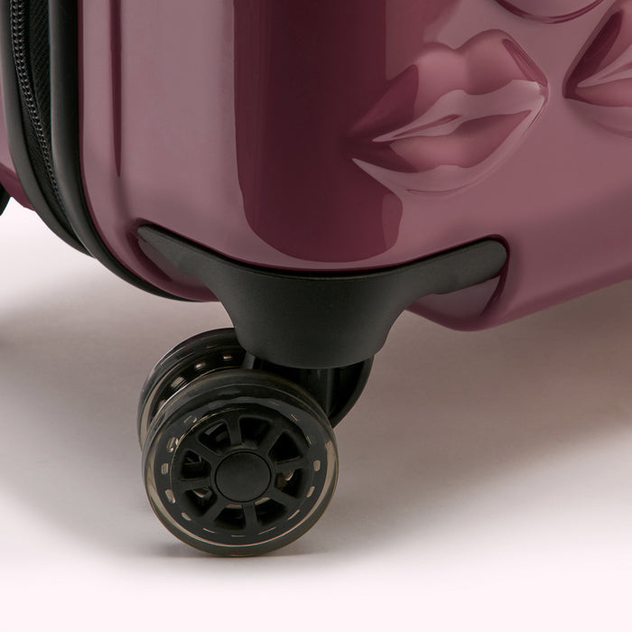 Close-up of a burgundy suitcase's wheels and base, featuring a unique lip design.
