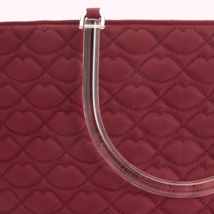 Close-up of a burgundy quilted handbag with a clear acrylic handle. The quilting is in a lip-shaped pattern.