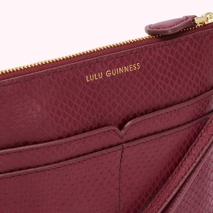 Close-up of a burgundy Lulu Guinness snakeskin-textured zip pouch with a gold zipper and strap.