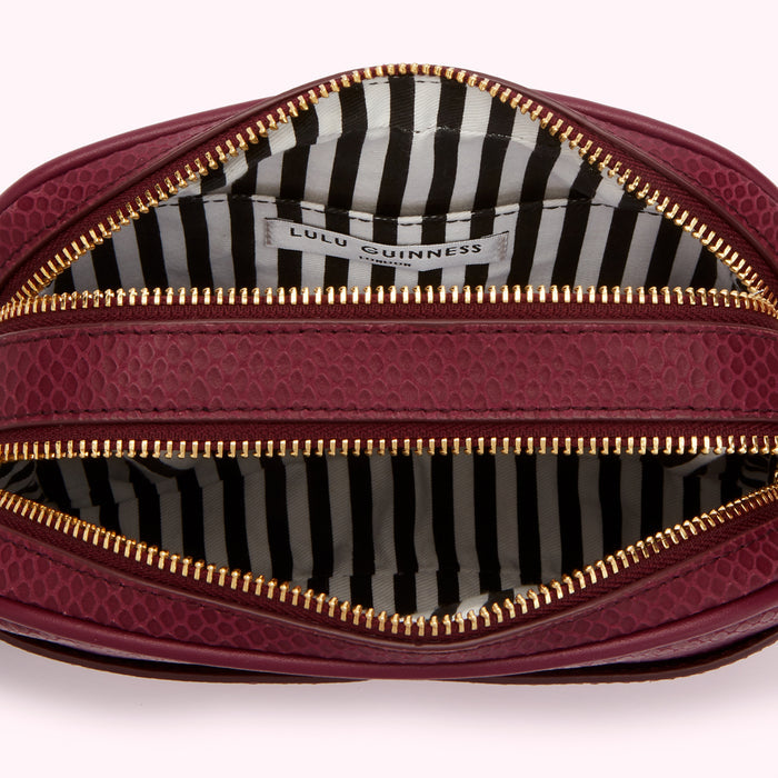 Interior of a burgundy Lulu Guinness purse with gold zippers and a black and white striped lining.
