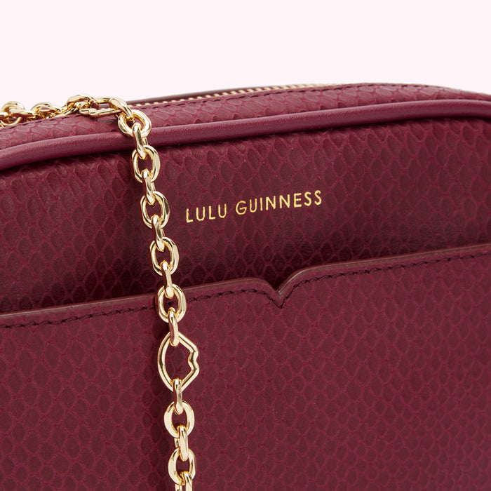 Close-up of a burgundy Lulu Guinness snakeskin crossbody bag with gold chain strap.