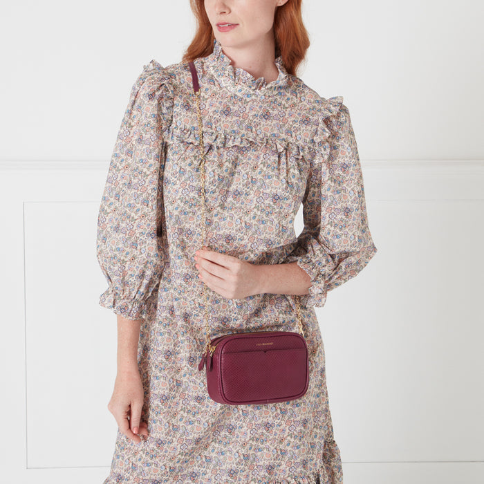 A woman in a floral dress carries a burgundy crossbody bag with a gold chain strap.