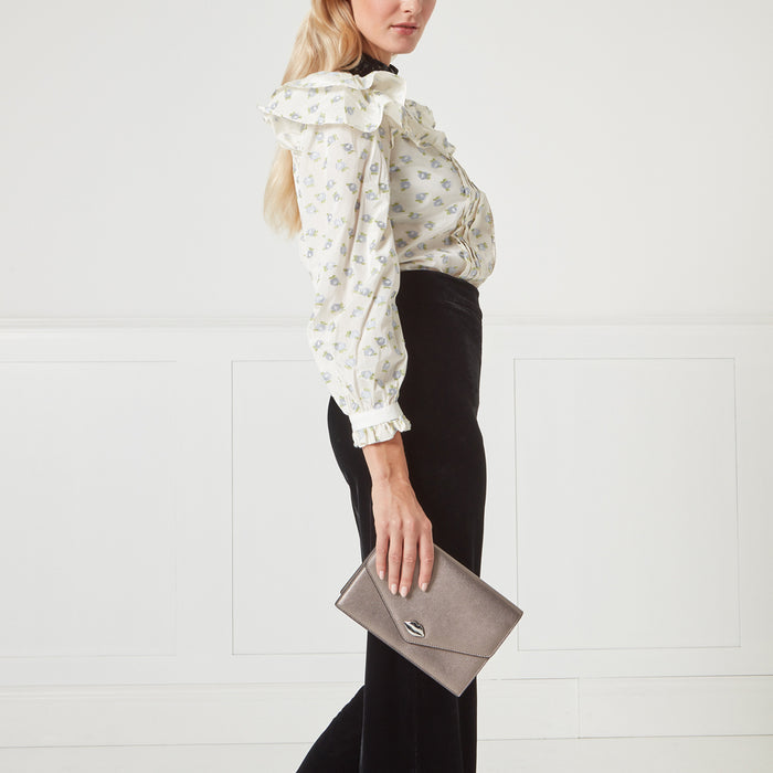 Woman in a floral blouse and black pants holding a metallic silver clutch.