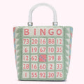 A pastel green tote bag with a clear handle features a bingo card design. The numbers are in pink, and the word "Bingo" is stitched at the top. The bag has a textured, possibly fuzzy, exterior.