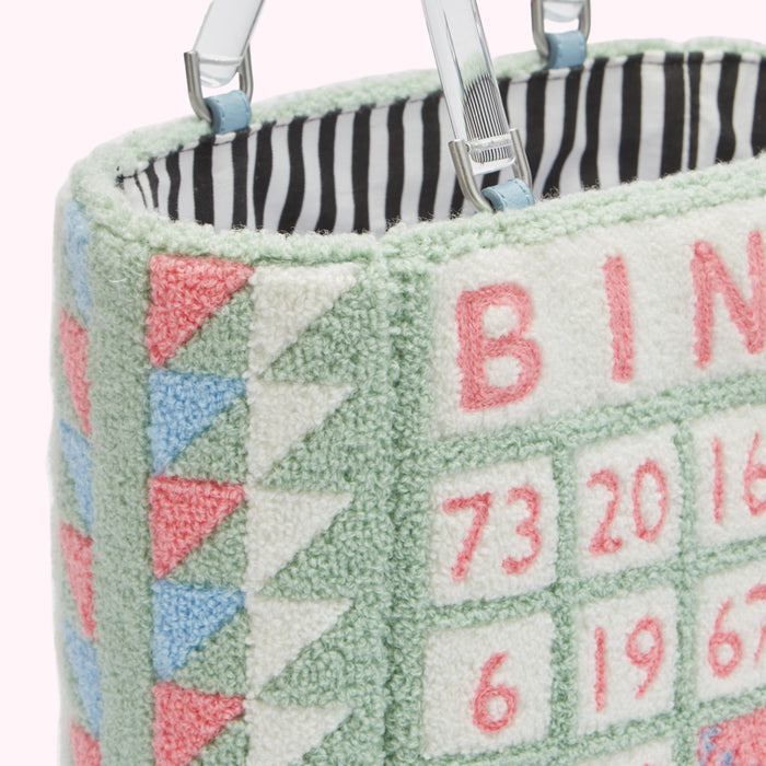 Close-up of a pale green fuzzy handbag with a Bingo-themed design; the numbers and letters are embroidered in pink.