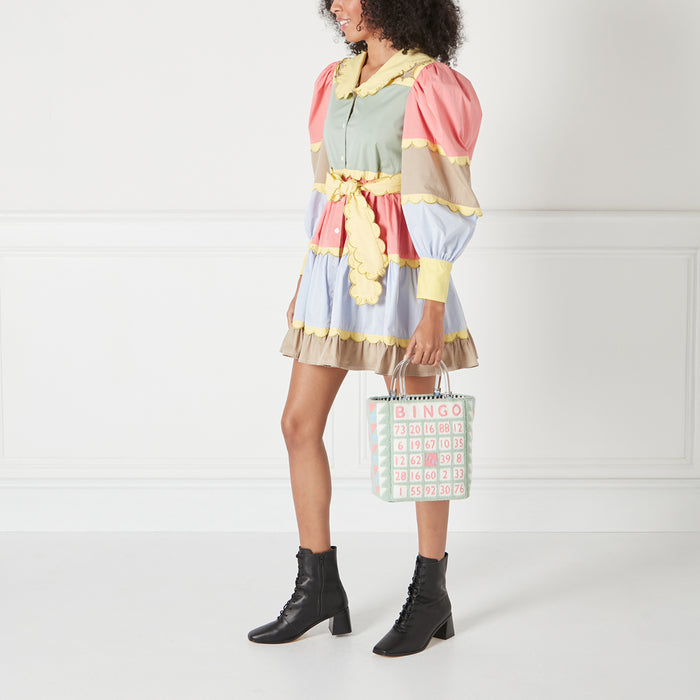 A woman in a pastel-coloured mini dress holds a pastel green bingo-themed tote bag against a white background.