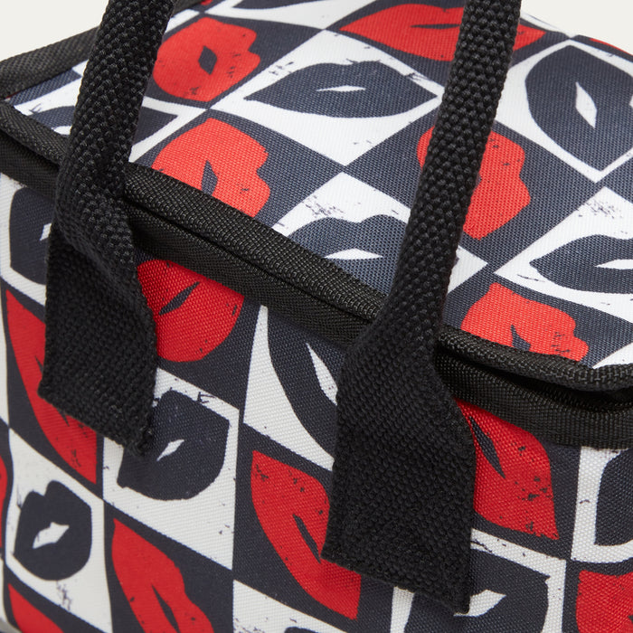 Close-up of a lunch bag with black webbed handles and a geometric lip print in red, black, and white.