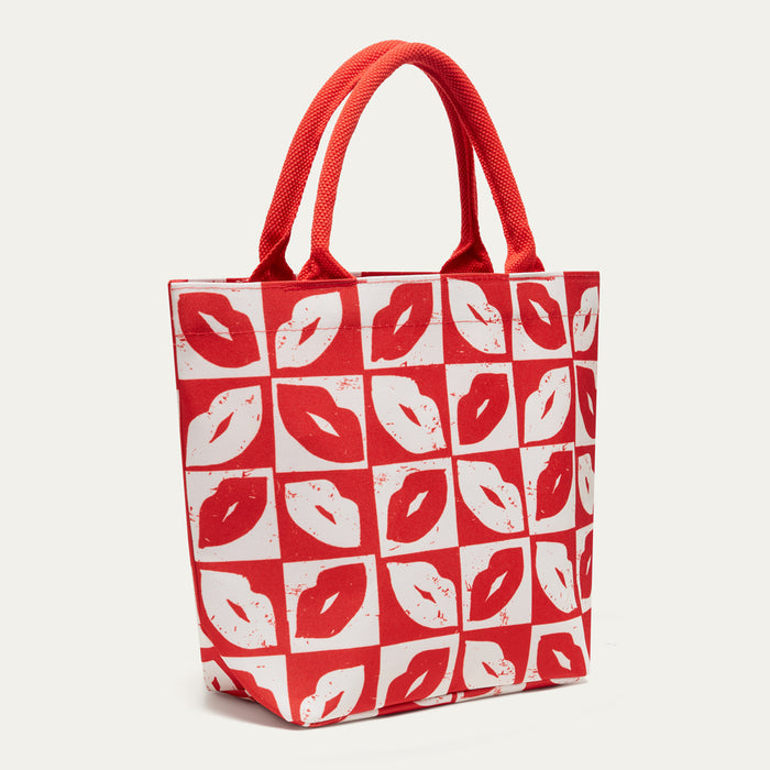 A red and white tote bag featuring a repeating pattern of lips in red and white on a checkered background, with two red handles, shown against a light off-white background.