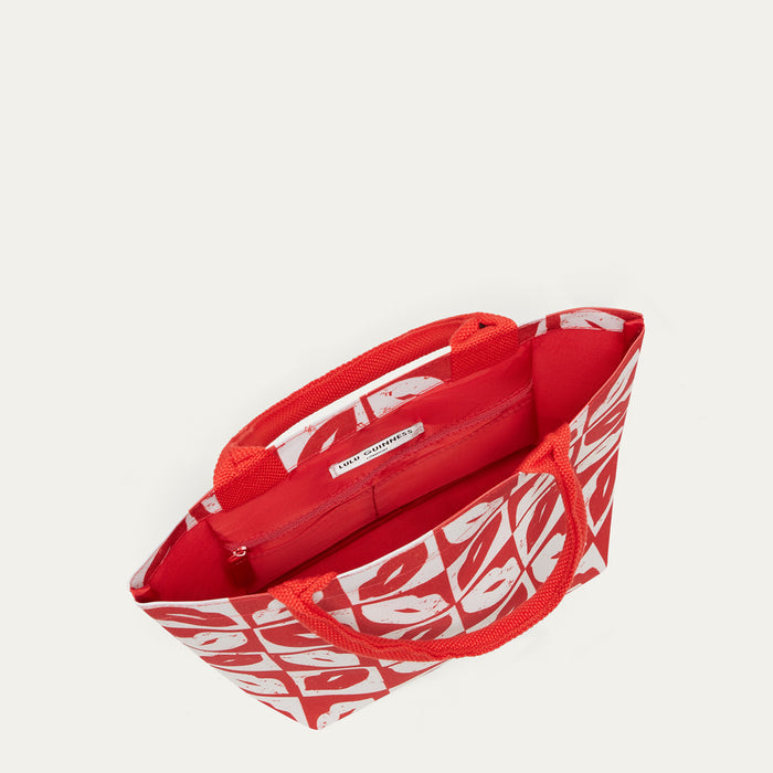 A red tote bag with a white abstract pattern and red rope handles, shown from an overhead angle on a light beige background.