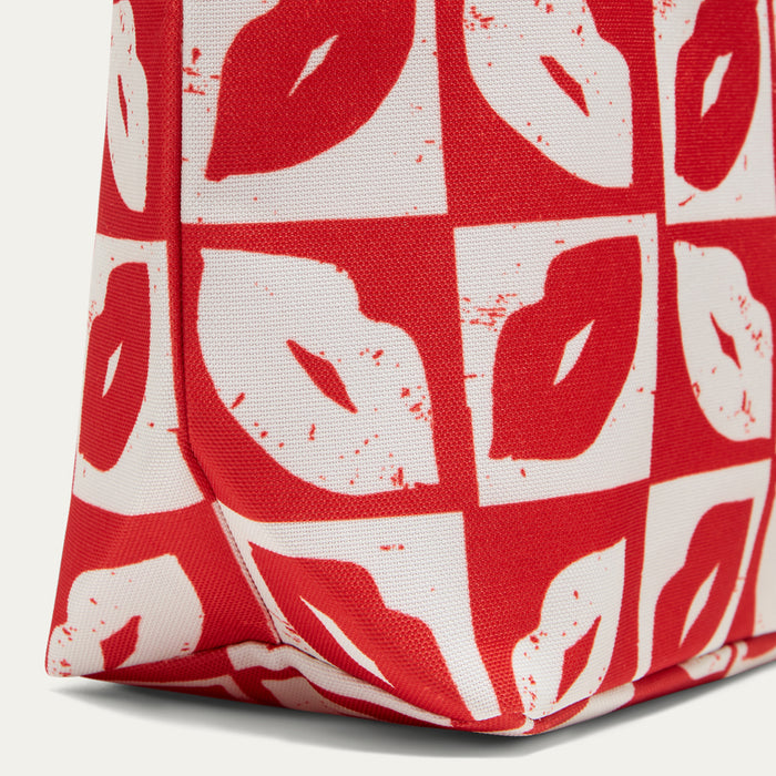 A close-up of a red and white patterned tote bag featuring a bold lip print in a checkerboard design.
