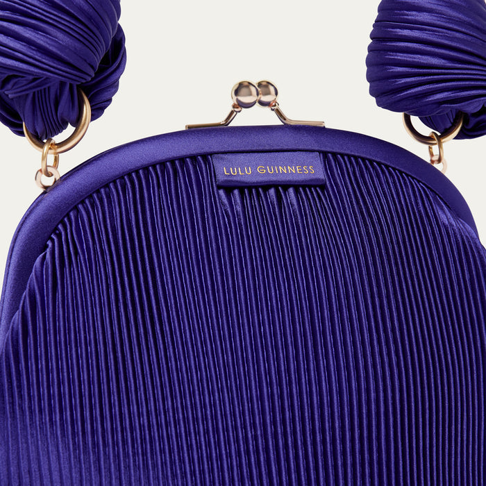 Purple pleated satin handbag with 'Lulu Guinness' branding on a light beige background