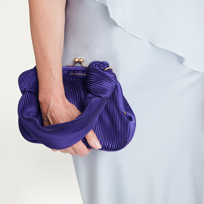 Purple pleated clutch held by a hand against a light gray background