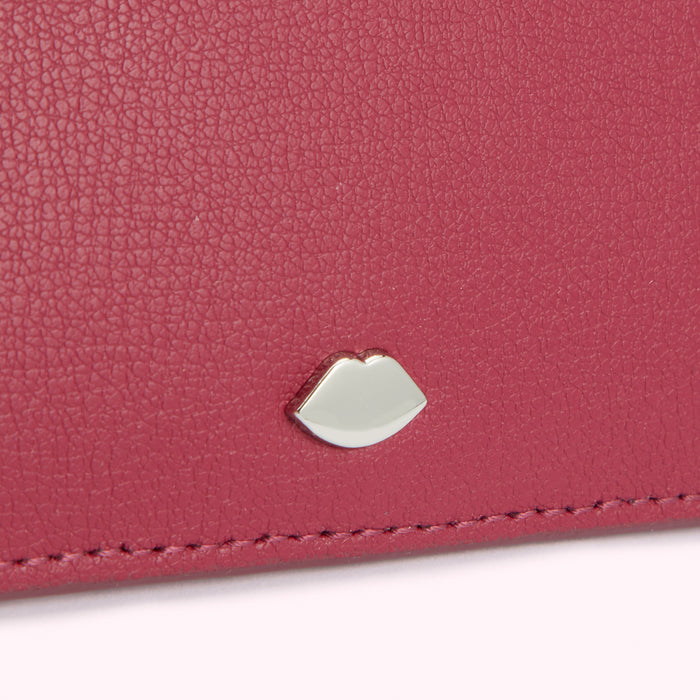 Close-up of a dark pink leather wallet with a silver lip-shaped emblem.